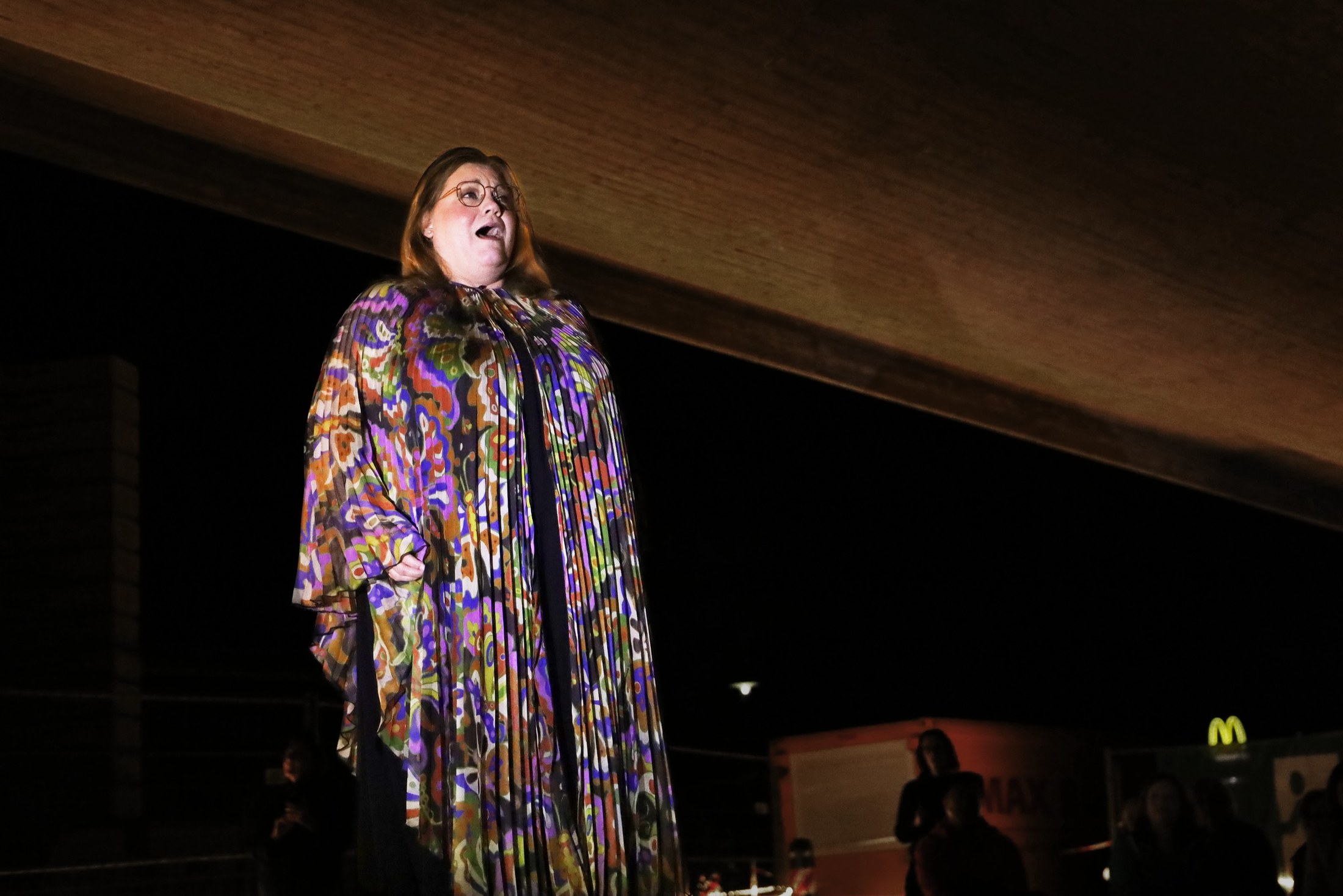 A singer in a long iridescent coat sings outdoors at night.