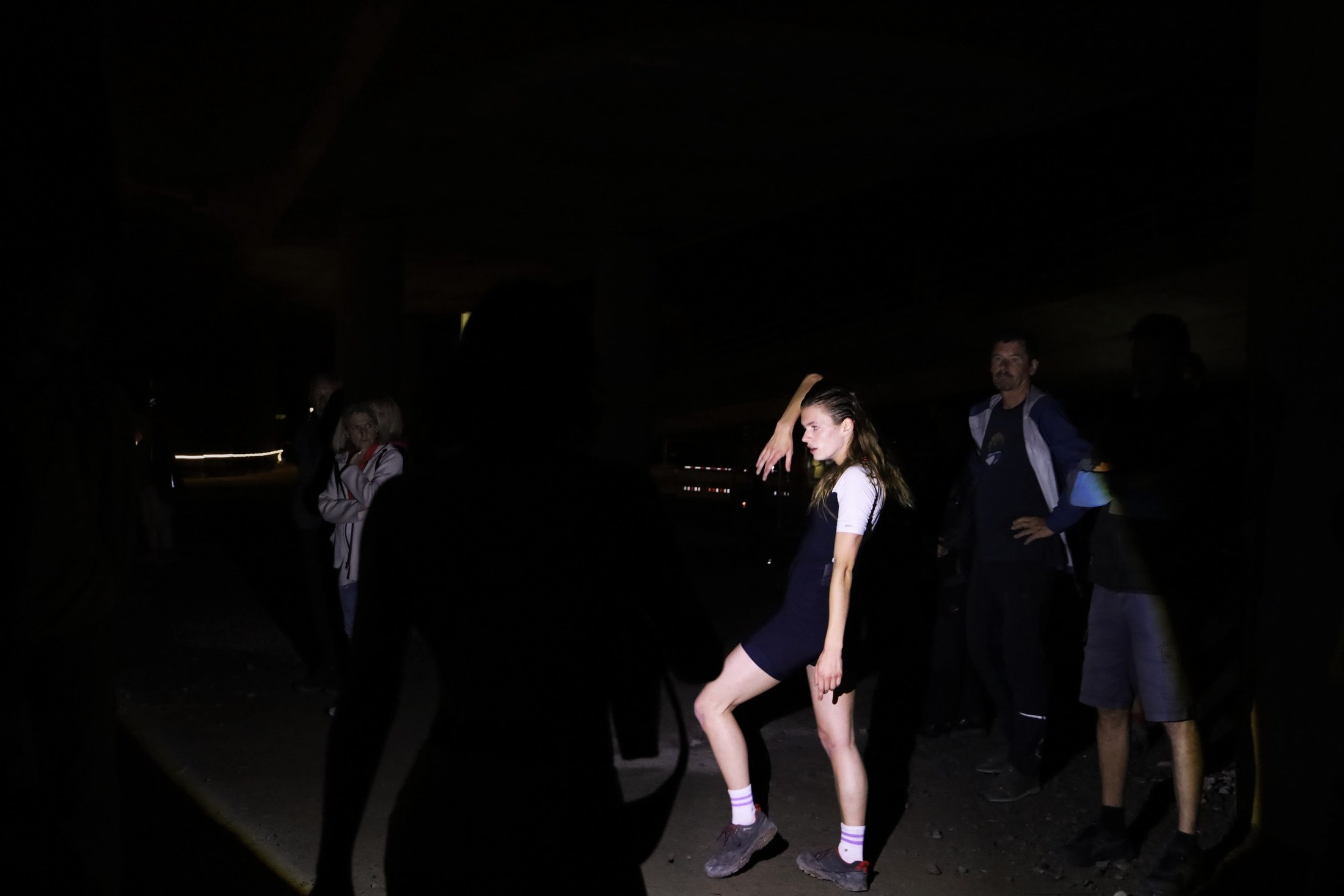 A performer dances in near-darkness among standing spectators.