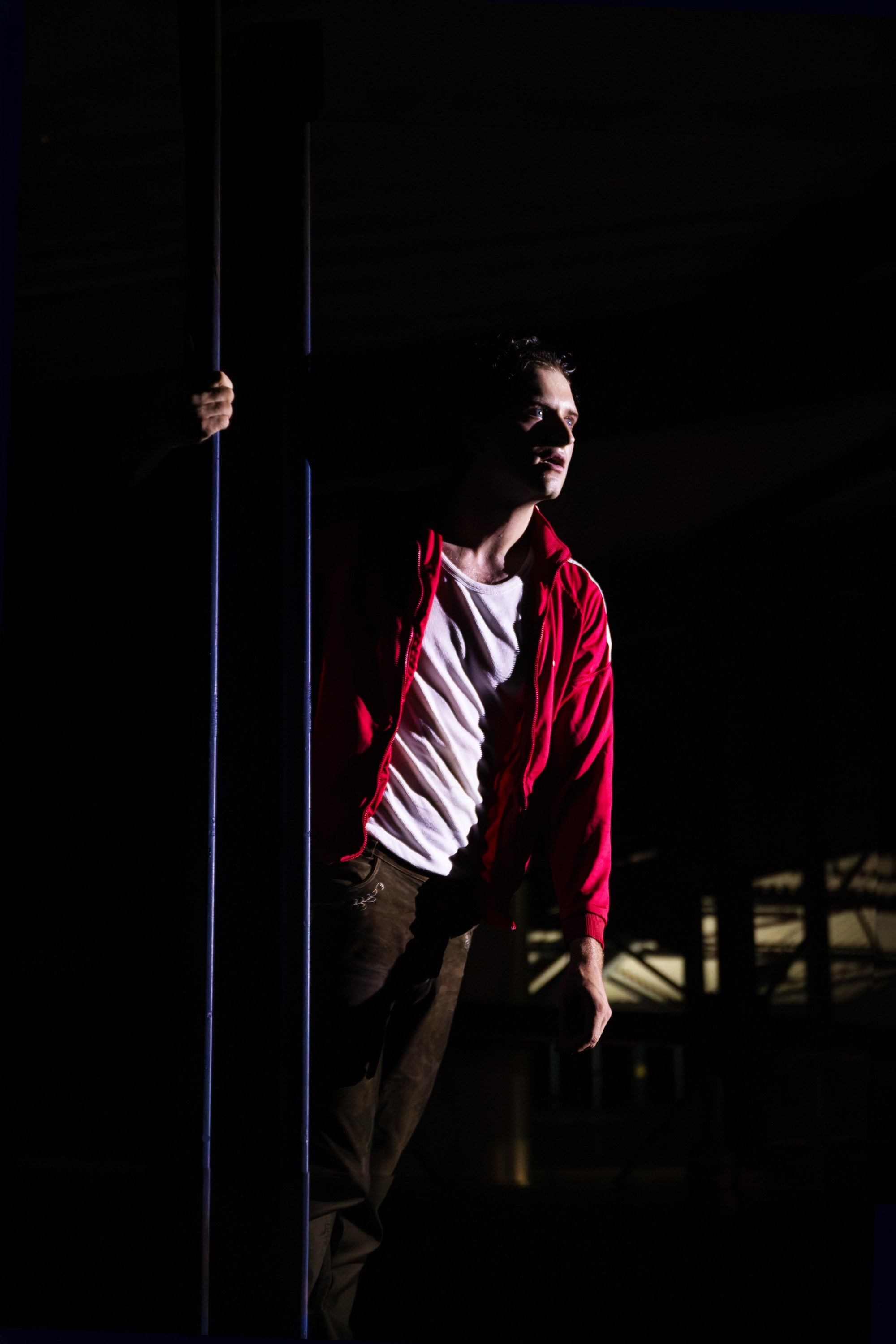 Hendrik Arns in a red jacket, lit from the side, holding a pole in a dark hall.