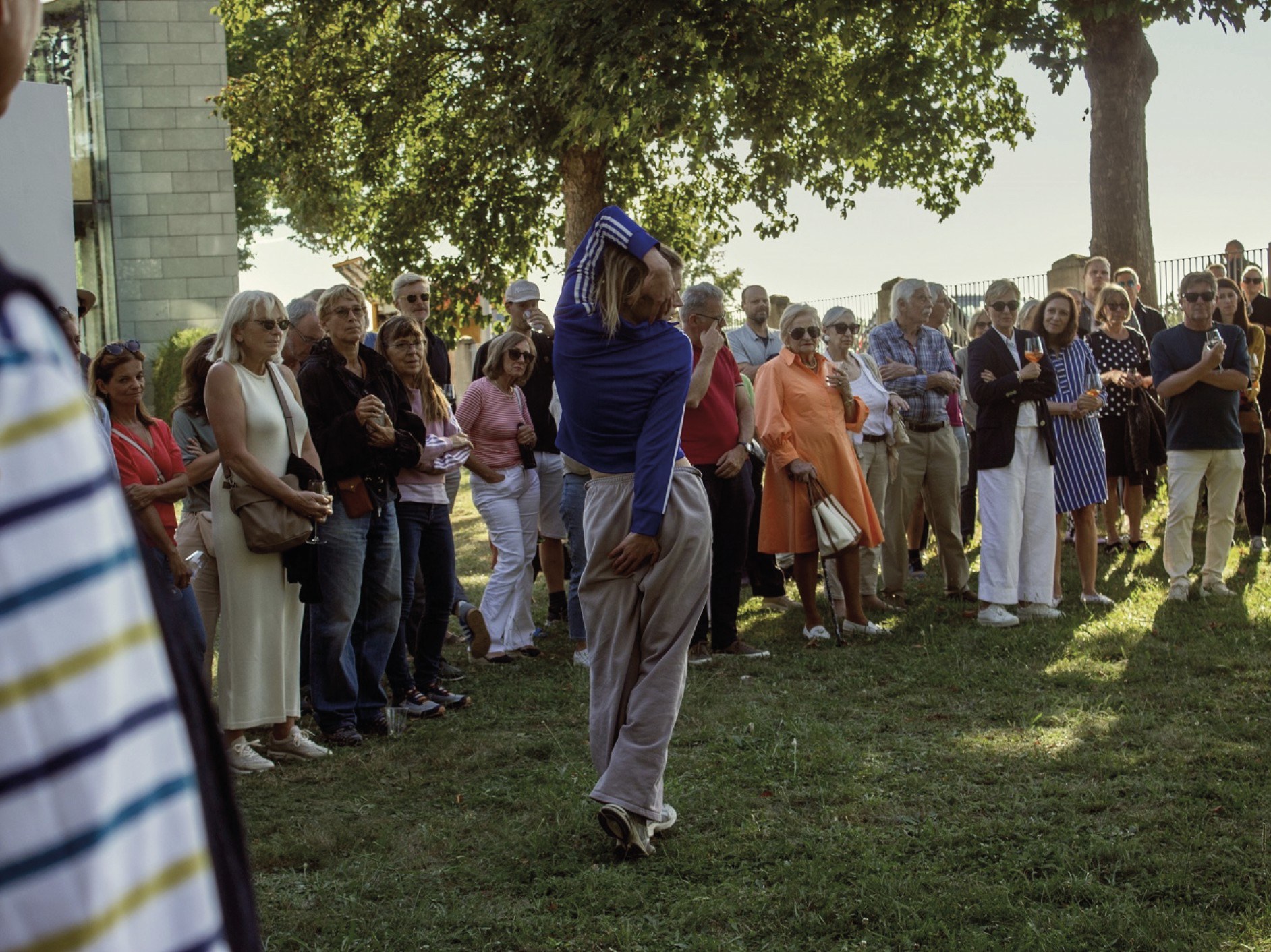 A performer moves through a standing crowd outdoors under trees.