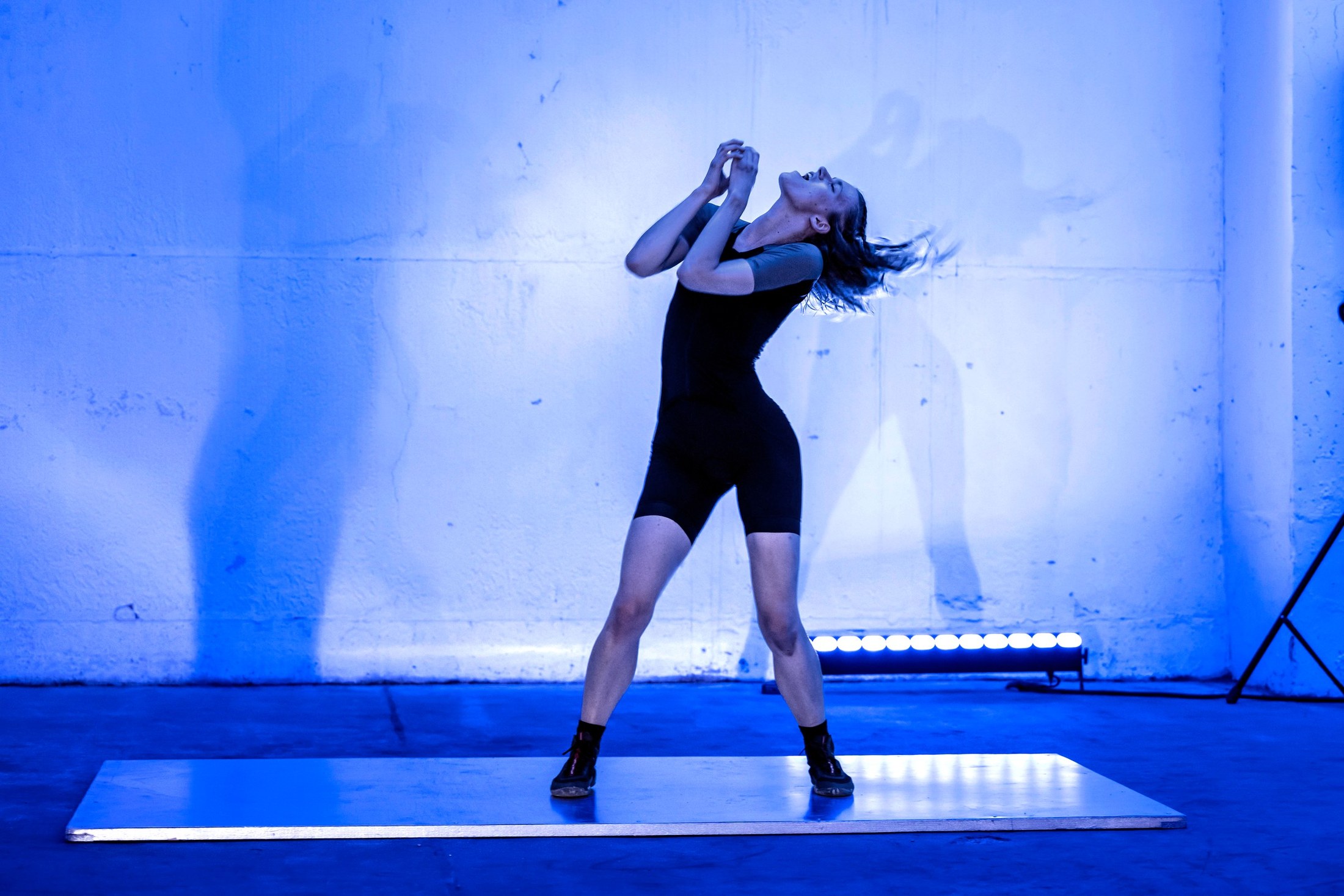 A dancer arches backwards on a lit mat in blue light.