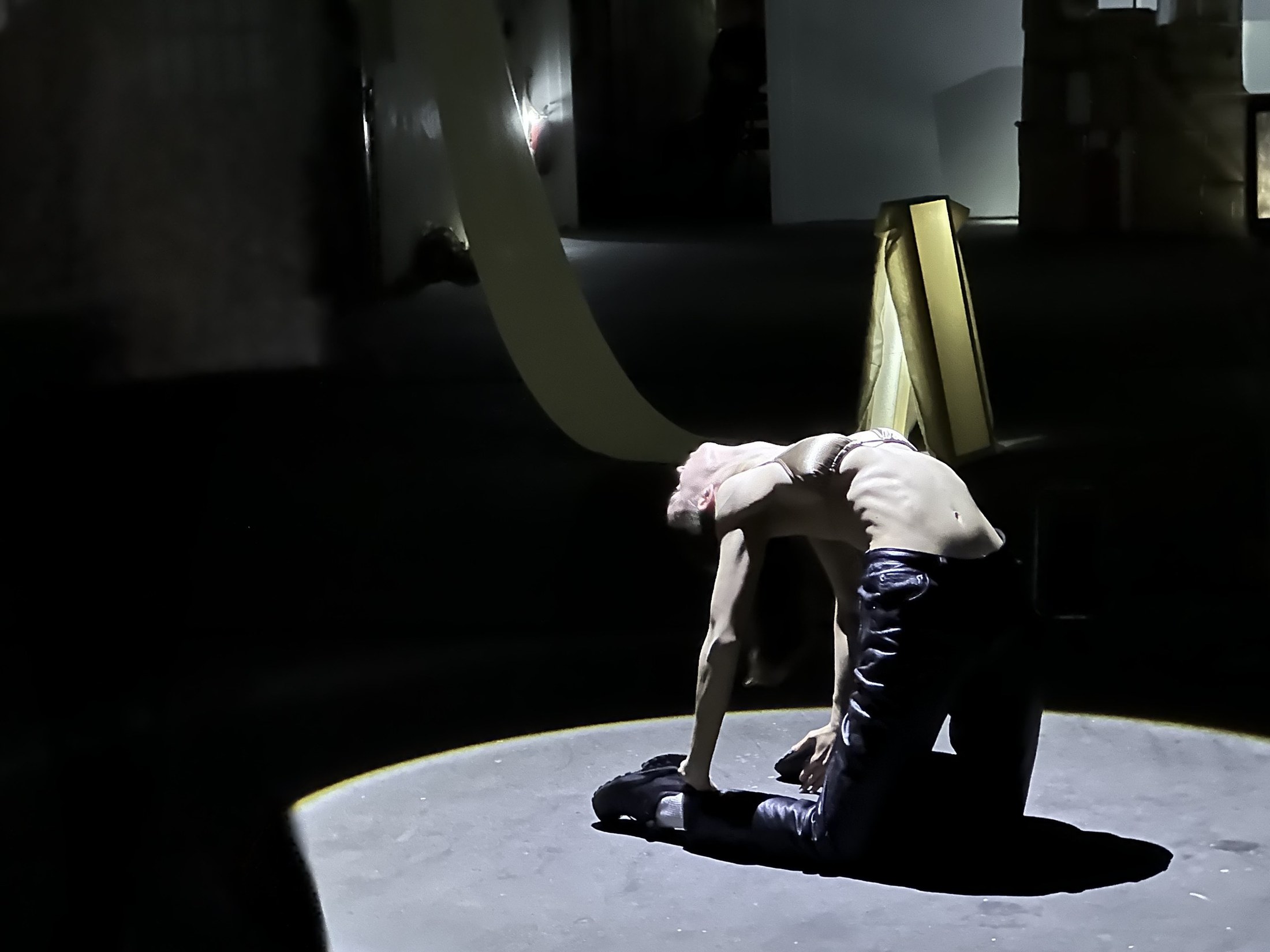 A performer bends backwards over a white plinth in a spotlight.