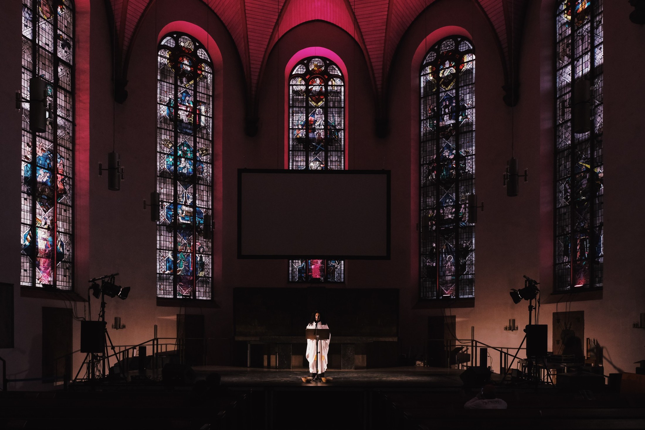 The nave of St. Katharinenkirche lit pink, a single figure at a lectern in front of a large screen.