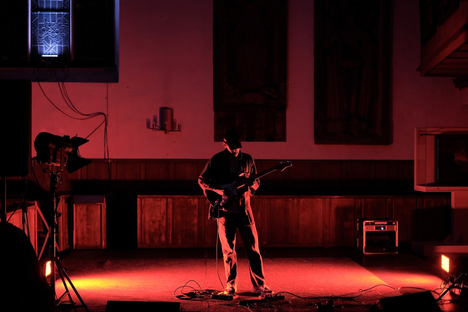 A guitarist silhouetted on a red-lit stage inside the church.