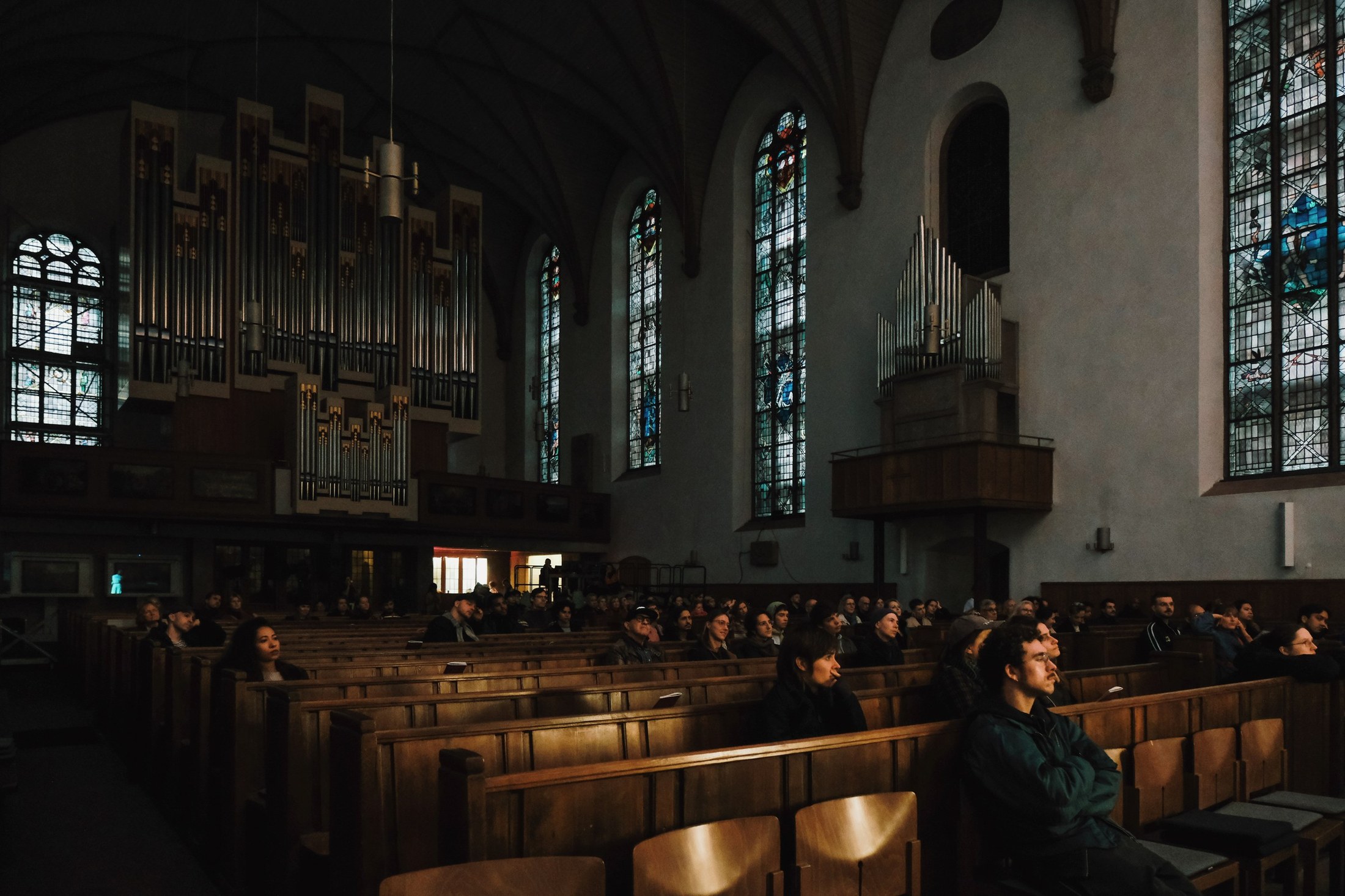 The audience sits in the church pews, organ pipes above them.