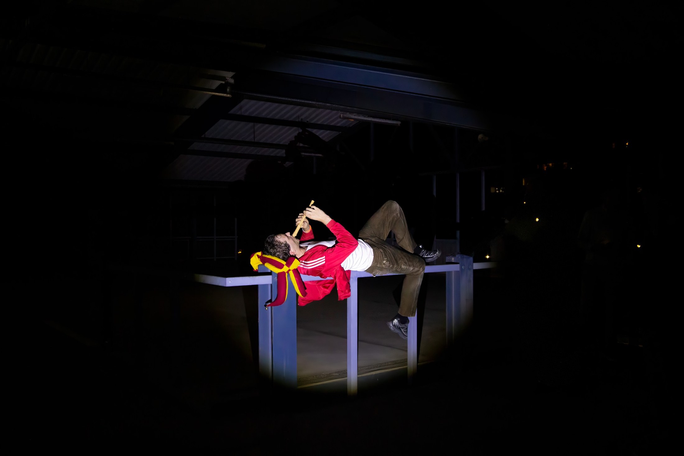 A performer in red reclines across a lit table in a dark hall.